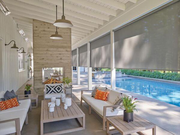 Exterior roller shades halfway drawn on a poolside patio
